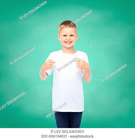 childhood, gesture, education and advertisement concept - smiling boy in t-shirt pointing his fingers at himself over green board background