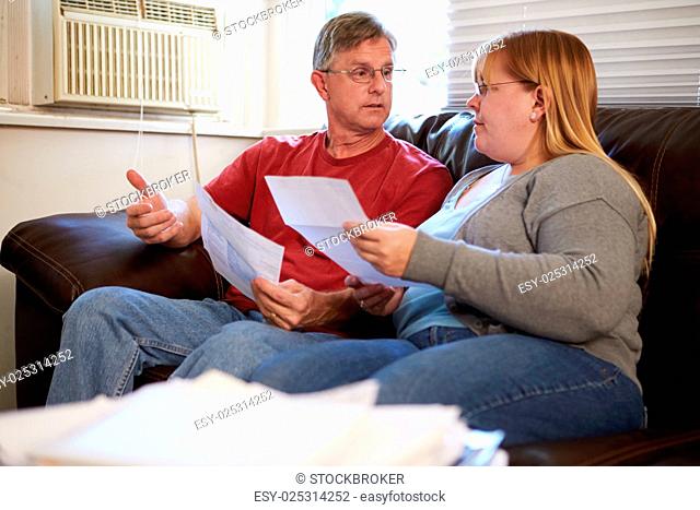Worried Couple Sitting On Sofa Looking At Bills