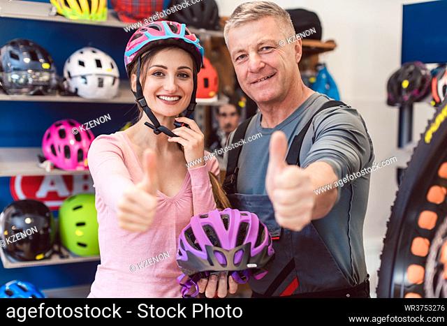 Customer choosing bicycle helmet in a shop with help from the owner