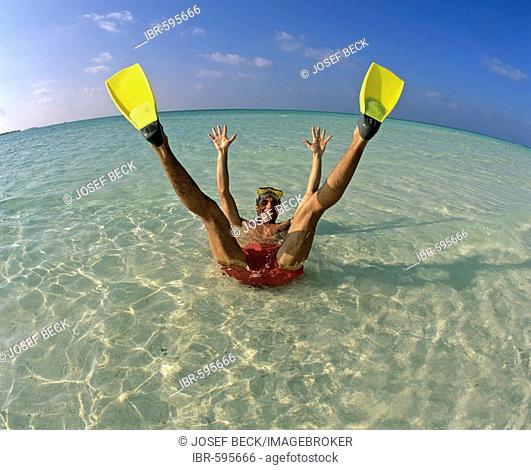 Young man wearing flippers laying in shallow water, vacation, Maldives, Indian Ocean