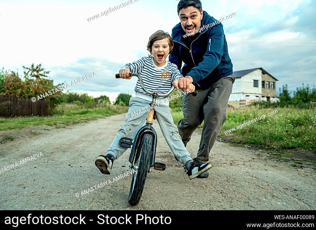 Father teaching son to ride bicycle on road