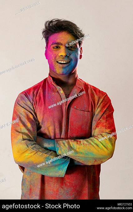 Young man smiling with colors all over him and folded hands on Holi