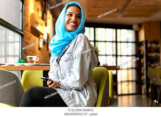Young woman wearing turquoise hijab and using smartphone in a cafe