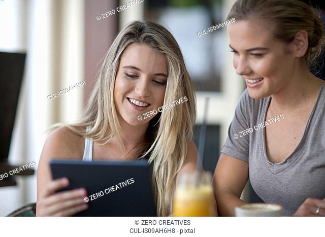 Two young adult female friends looking at digital tablet in cafe
