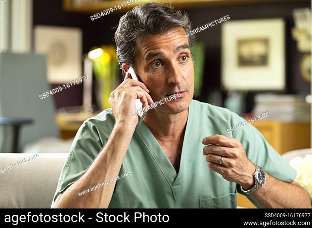 Hispanic Male doctor practicing tele-medicine from his home office, Talking to patient on cell phone