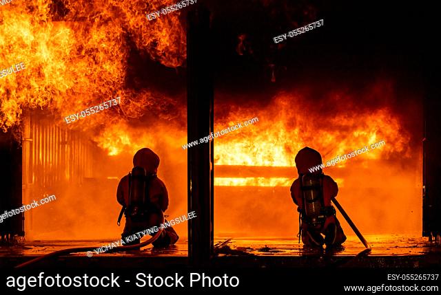Firefighters using water fog fire extinguisher to fighting with the fire flame in large building. Firefighter and industrial safety disaster and public service...