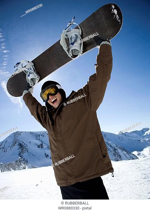 Low angle view of a young man lifting a snowboard and shouting