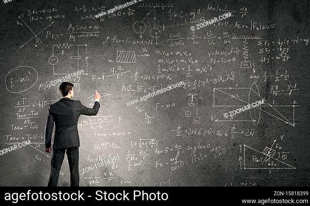 Man in suit standing with back and drawing physics formulas