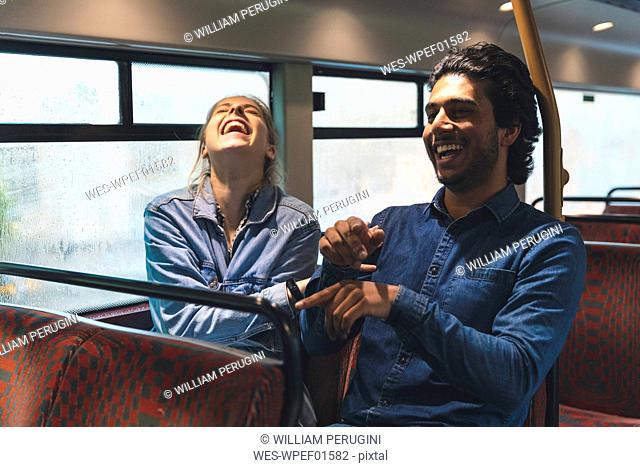 Young couple travelling by bus on rainy day having fun, London, UK