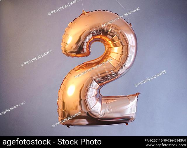 PRODUCTION - 14 January 2022, Berlin: ILLUSTRATION - A golden balloon in the shape of the number 2 hangs against a gray background