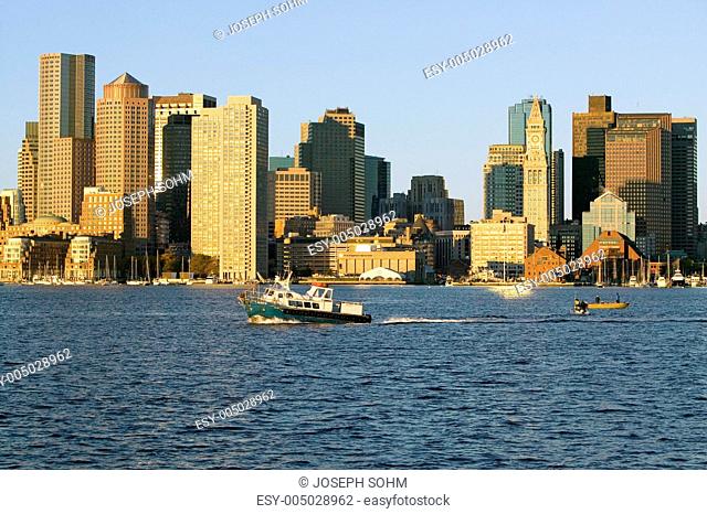 Boat travels in front of Boston Harbor and the Boston skyline at sunrise as seen from South Boston, Massachusetts, New England