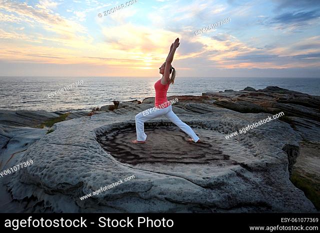 A female lunges forward while stretching the other leg and arms straight above her head as a yoga pilates routine by the sea
