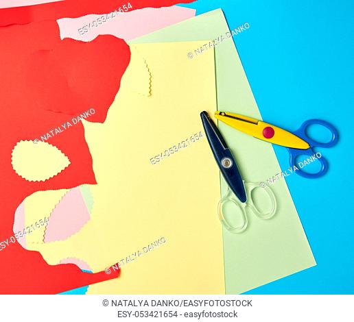 pair of plastic scissors and colored paper for cutting figures, application and scrapbooking