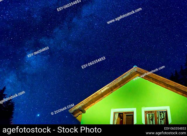 Green house under dark blue night sky with many stars, cosmos milky way background