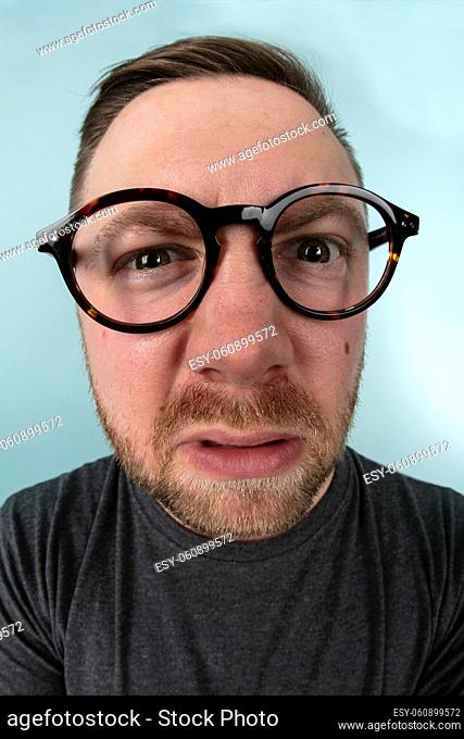 Man wearing large glasses stretching forwards to peer into the lens in a distorted perspective emphasising his eyes and glasses in a fun portrait