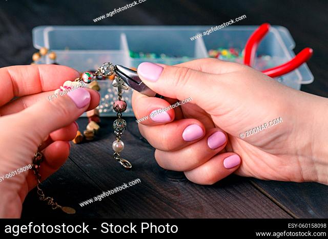 Woman making beads. Box with beads, spool of thread, plier and glass hearts to create hand made jewelry on old wooden background