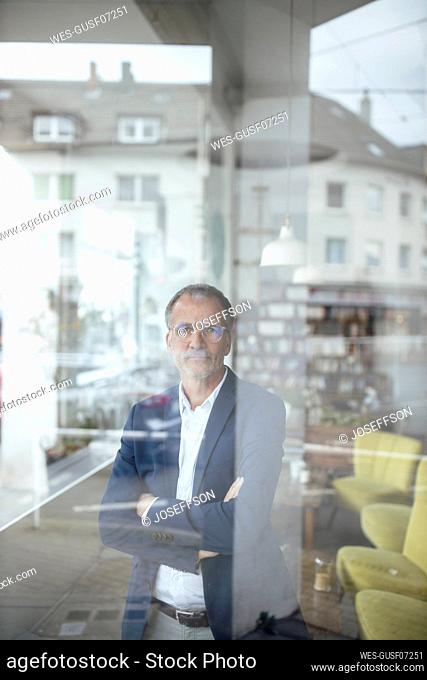 Businessman with arms crossed seen through glass window at cafe