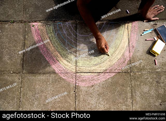 Arms of adult woman drawing crayon rainbow on pavement