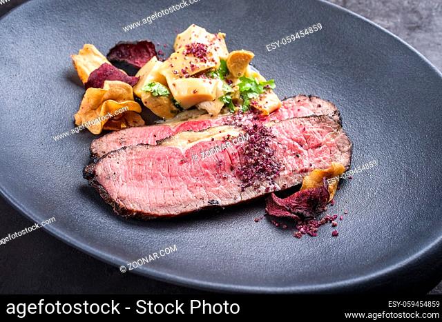 Modern style Commonwealth Sunday roast with sliced cold cuts roast beef, pickled mushrooms and vegetable chips offered as close-up on a cast-iron design plate