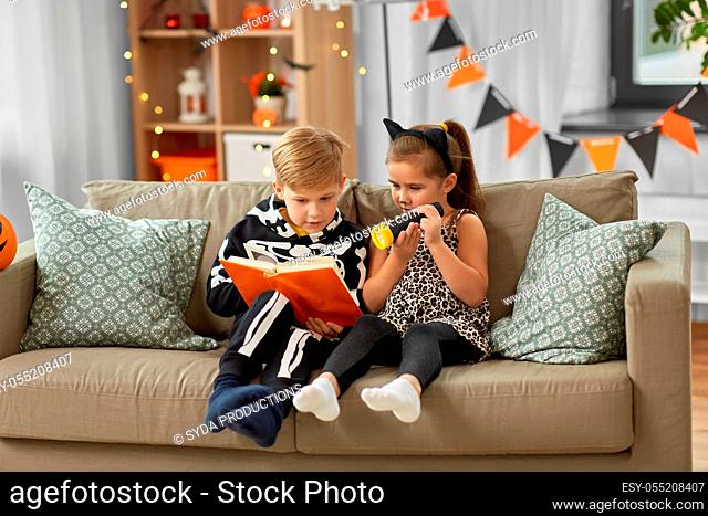 kids in halloween costumes reading book at home