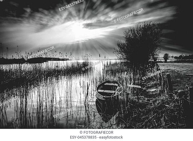 Old landscape with vintage rowing boat in a reed collar with atmospheric and intense sunset. Old pollard willows and drawn cloudy skies with sunbeams scorch the...