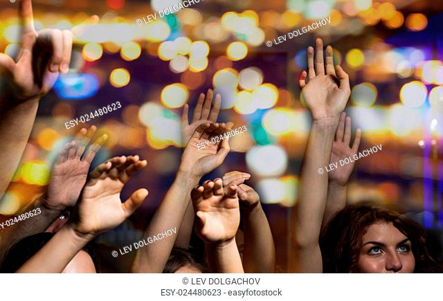 party, holidays, music, nightlife and people concept - close up of happy people at concert in night club waving hands
