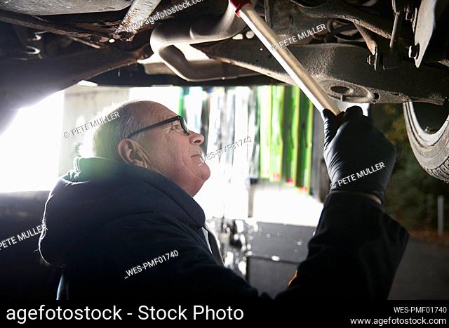 Male auto mechanic repairing car in shop
