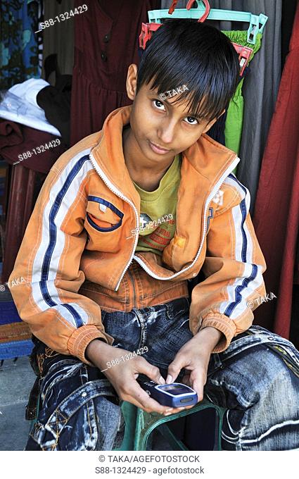 Boy holding mobile phone sitting at the shop in New Manali shopping street. Manali, Himachal Pradesh, India
