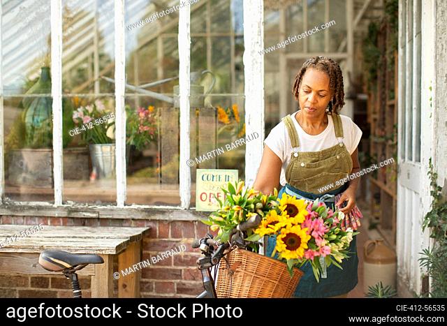 Female florist placing flowers in bicycle basket outside shop