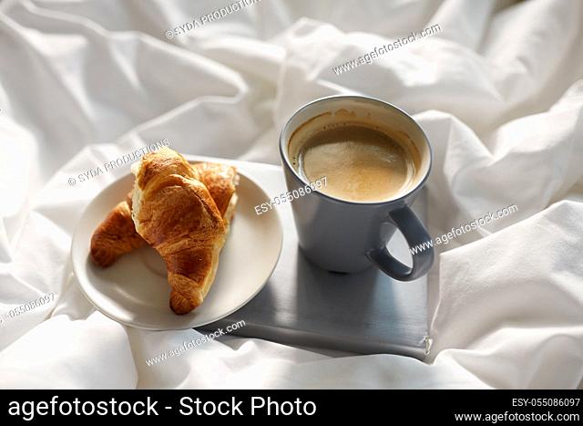 croissants, cup of coffee and book in bed at home