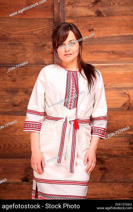 Pretty Ukrainian girl dressed in traditional costume embellished with embroideries. Woman with dark thick hair isolated on wooden background