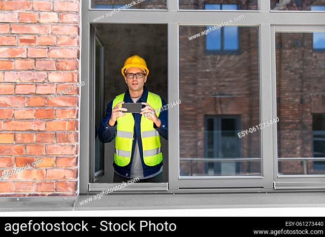 builder with smartphone taking picture at window