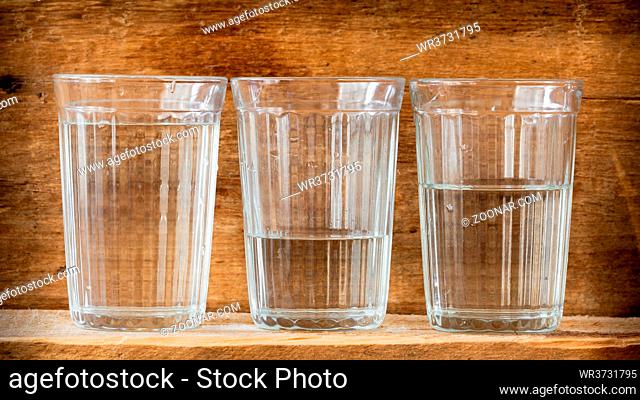 Three glasses of water, illuminated with natural light, on a wooden plank