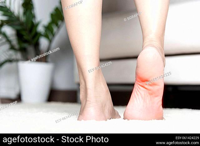 Foot pain, Asian woman standing feeling pain in her foot at home, female suffering from feet ache use hand massage relax muscle from soles in home interior