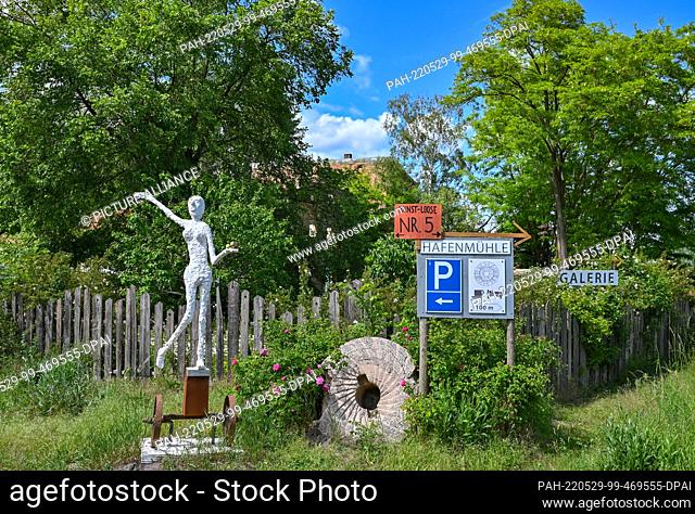 28 May 2022, Brandenburg, Kienitz: An old millstone and a sculpture stand in front of the fence of the cafe, gallery and vacation apartment of the Hafenmühle...