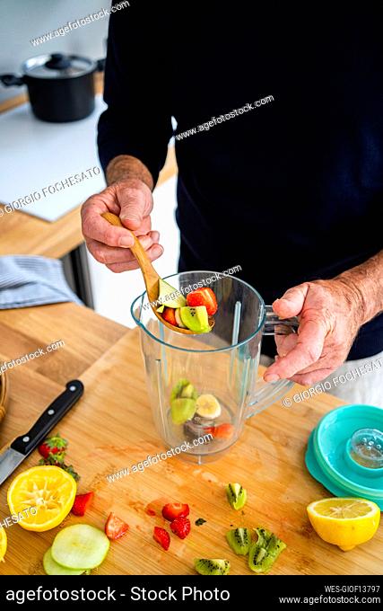 Man putting chopped fruits in juicer at kitchen counter