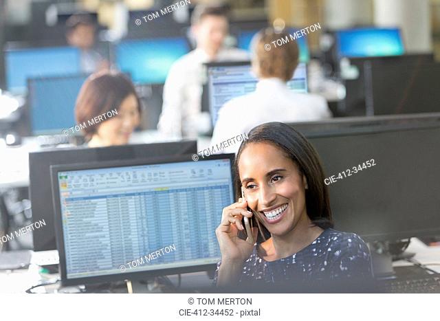 Smiling businesswoman talking on cell phone at computer in office