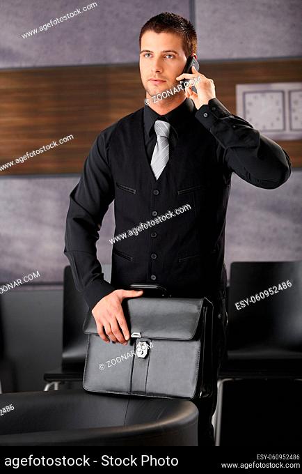 Handsome businessman standing in office lobby, talking on mobile phone