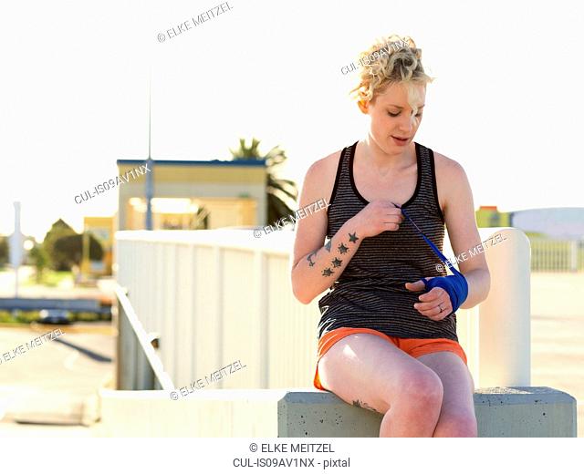 Young female boxer wrapping hands in bandage at parking lot