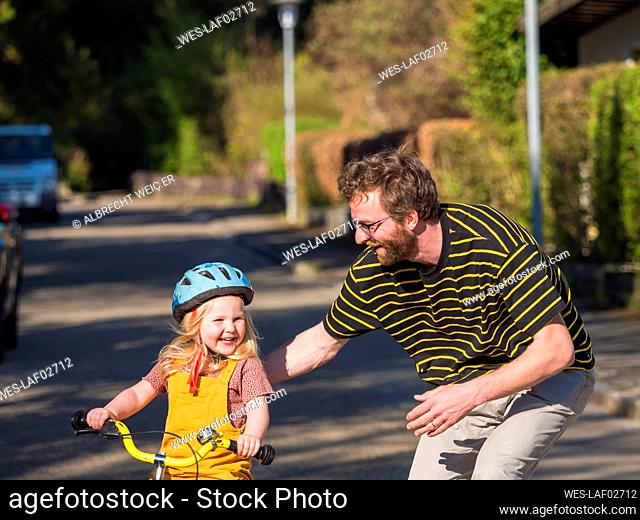Happy father teaching cycling to daughter outdoors