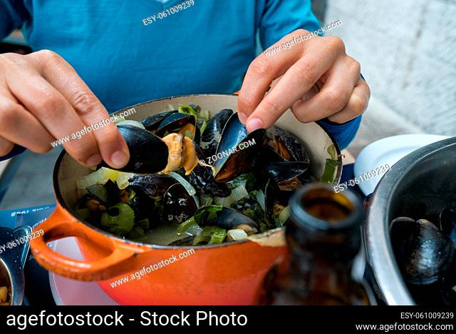 Horizontal view of hands of a woman eating traditional mussel and french fries dish called