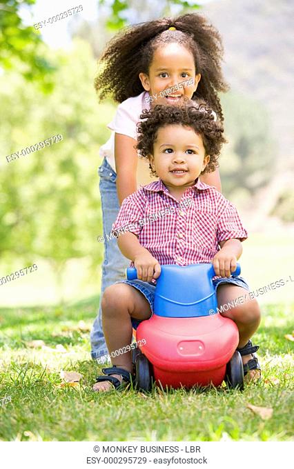 Sister pushing brother on toy with wheels smiling