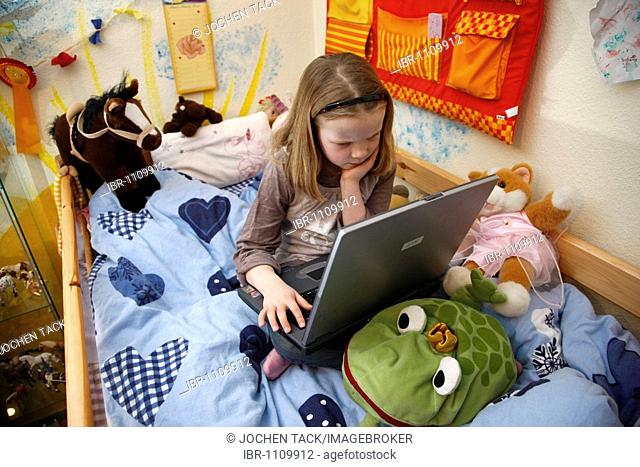 Girl, 7 years old, working with a computer at home in her room, sitting on her bunk bed, doing homework for school, educational software