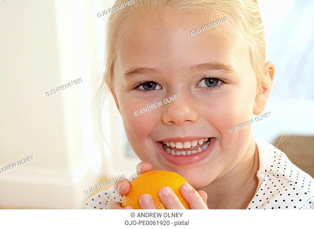 Young girl in kitchen holding orange and smiling