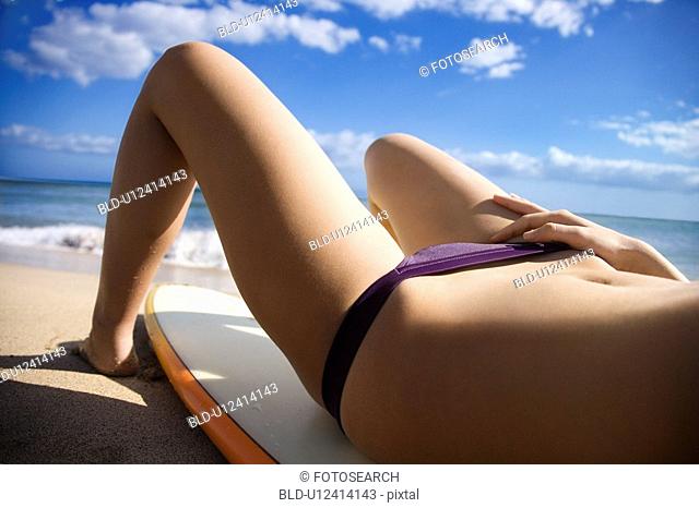 Woman in bikini lying on surfboard
