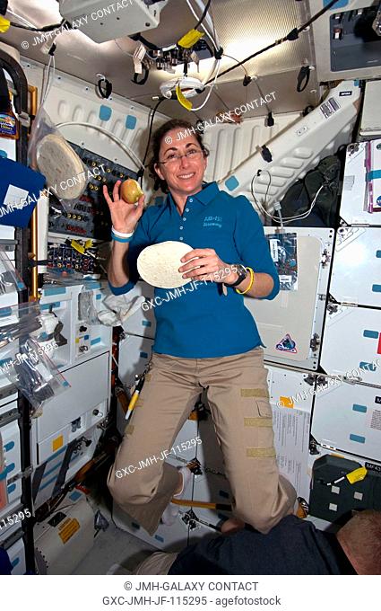 On space shuttle Discovery's middeck, astronaut Nicole Stott, STS-133 mission specialist, enjoys a flight day 2 snack. She is holding an apple and a tortilla