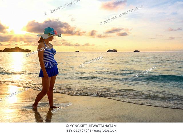Girl in blue swimsuit walking on beach with happy and beautiful sky above the sea during sunrise at Honeymoon Bay, Koh Miang Islands, Similan National Park