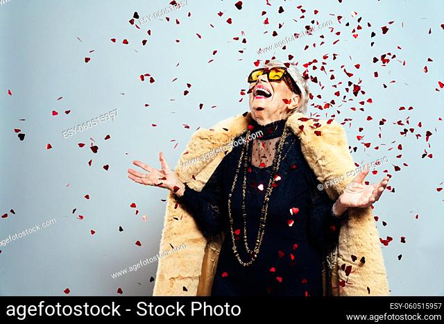 image of a beautiful and elegant old influencer woman. Cool grandmother posing in studio wearing fashionable clothes. Confetti explosion on her 90s birthday...