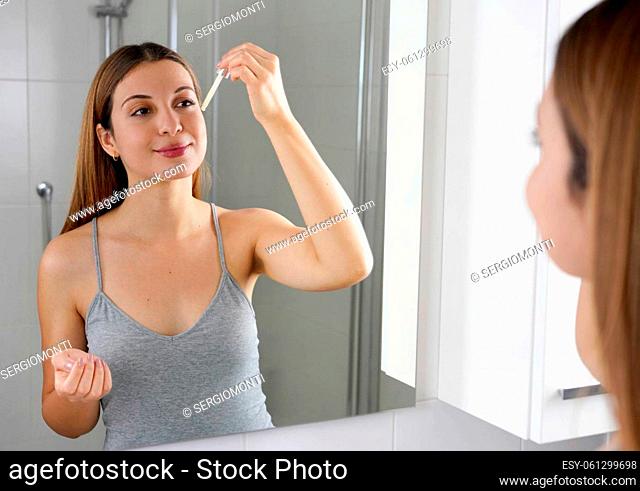 Young Skin Care Routine. Beautiful girl applying a Vitamin C booster antioxidant ascorbic acid anti aging serum to her face while holding a pipette in her hand