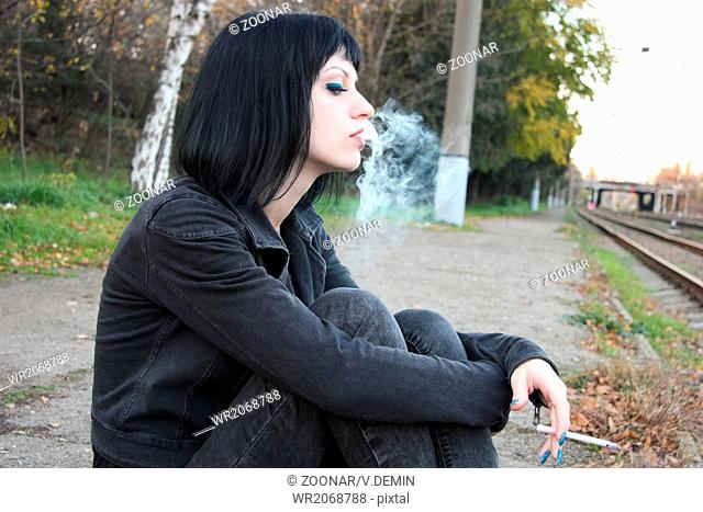 Girl sit and smoke near rails